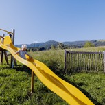 Kind auf gelber Wellenrutsche am Spielplatz, Puradies Leogang