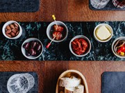Tapas-Auswahl auf grünem Marmor im Restaurant Ess:enz – Naturresort Puradies Leogang Draufsicht auf Tapas-Schälchen mit Mandeln, Oliven, Speckspieß, Tomatendip, Butter und Peperoni auf grünem Marmor sowie frisches Weißbrot im Restaurant Ess:enz, Puradies Leogang