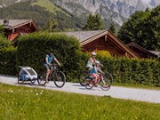 Familie mit Fahrradanhänger auf Radweg vor Bergpanorama – Naturresort Puradies, Leogang, Salzburger Land Familie mit Fahrradanhänger auf Radweg, Naturresort Puradies in Leogang