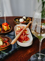 Tapas mit Schinken und Grissini im Restaurant Ess:enz – Naturresort Puradies Leogang Rohschinken mit Grissini auf grünem Marmor, dazu Tomatensalat, gefüllte Paprika und ein Glas Weißwein im Restaurant Ess:enz, Puradies Leogang