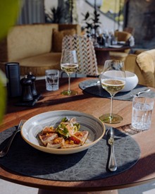 Angerichtetes Gericht mit Weißwein am gedeckten Tisch, Puradies Leogang
