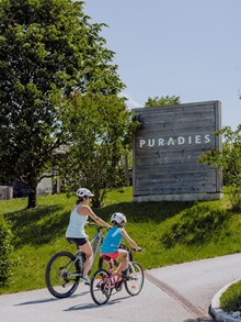 Erwachsener und Kind auf Fahrrädern beim Puradies-Schild – Naturresort Puradies, Leogang, Salzburger Land Erwachsener und Kind auf Fahrrädern beim Puradies-Schild, Leogang