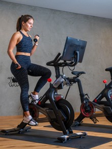 Person am Peloton-Bike mit Kurzhanteln im Fitnessraum, Naturresort Puradies in Leogang