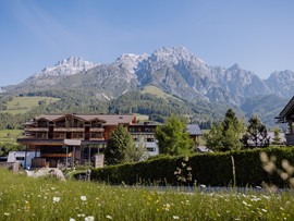 Haupteingang hinter Blumenwiese vor Bergpanorama, Puradies Leogang