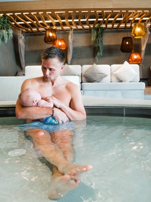 Kinderpool Heaven Spa – Vater und Kind am Wasser Vater sitzt mit Kleinkind am Rand des Kinderpools im Heaven Spa, im Hintergrund Loungebereich mit hängenden Pflanzen und Wasserrutsche