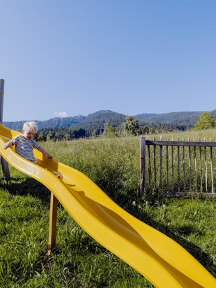 Kind an der gelben Rutsche am Abenteuerspielplatz, Naturresort Puradies, Leogang, Salzburger Land Kind auf gelber Wellenrutsche am Spielplatz, Puradies Leogang