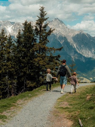 Person und Kindern spazieren auf Schotterweg mit Blick auf Leoganger Steinberge und Leogang Tal Person und Kindern spazieren auf Schotterweg mit Blick auf Leoganger Steinberge und Leogang Tal