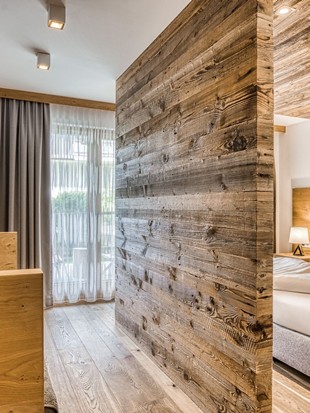 Sitzbank mit Blick auf Doppelbett hinter Altholzwand in der Deluxe Suite im Naturresort Puradies