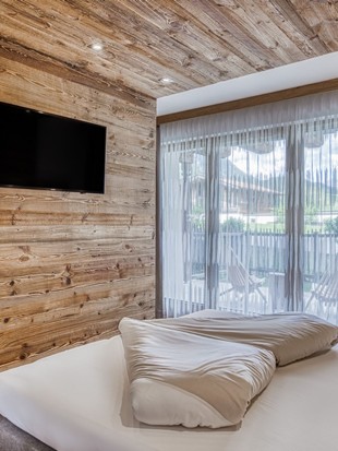 Doppelbett mit Fernseher und Terrassenzugang in der Deluxe Suite im Naturresort Puradies
