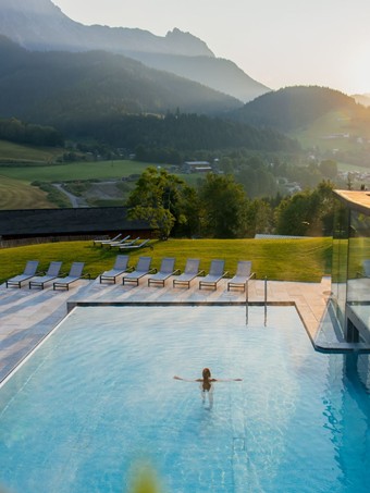 Person im Infinity Pool des Heaven Spa bei Sonnenaufgang, Puradies Leogang