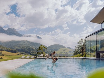 Mann hebt Kind hoch im Infinity Pool im Sommer, Puradies Leogang