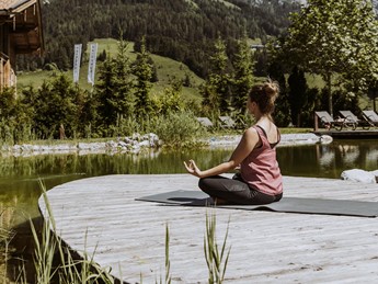 Meditation am Naturbadeteich mit Blick zum Bergpanorama – Naturresort Puradies, Leogang, Salzburger Land Person in Meditationshaltung am Naturbadeteich, Naturresort Puradies in Leogang
