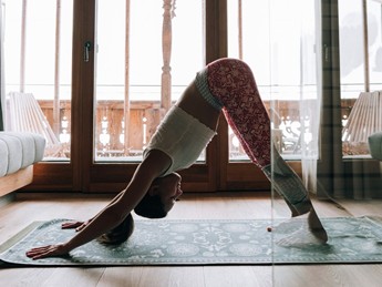 Yoga-Herabschauender-Hund im Zimmer mit Winterblick – Naturresort Puradies, Leogang, Salzburger Land Person in Yoga-Haltung herabschauender Hund im Zimmer, Naturresort Puradies in Leogang