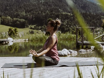 Person in Meditationshaltung am Naturbadeteich, Naturresort Puradies in Leogang