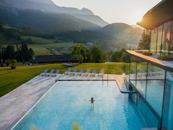 Person im Infinity Pool des Heaven Spa bei Sonnenaufgang, Puradies Leogang