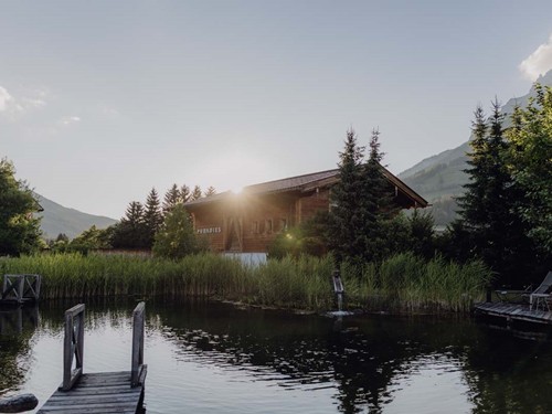 Natural Swimming Pond with Sauna House in Warm Evening Light – Naturresort Puradies, Leogang, Salzburger Land Natural Swimming Pond with Sauna House in evening light, Puradies Leogang