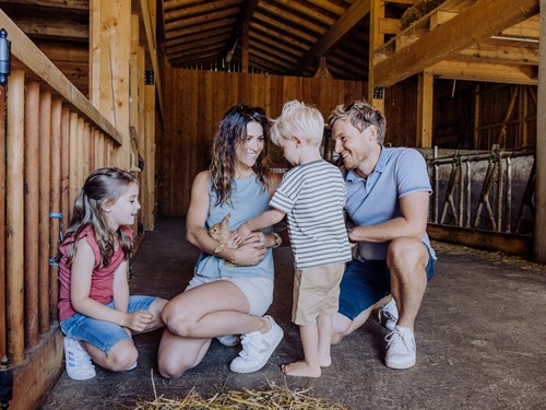 Two adults and two children crouch in the organic farm, lifting and petting a rabbit.