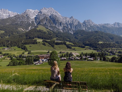 Zwei Wanderinnen auf Aussichtsbank mit Blick auf das Hotel – Naturresort Puradies, Leogang, Salzburger Land Zwei Wanderinnen auf Bank mit Blick auf das Hotel, Naturresort Puradies in Leogang