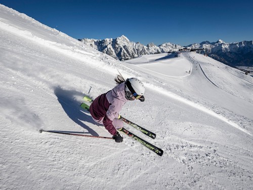 Skifahrerin in dynamischer Kurve auf Piste mit Bergpanorama – Naturresort Puradies, Leogang, Salzburger Land Skifahrerin in Kurve mit Bergpanorama, Naturresort Puradies in Leogang