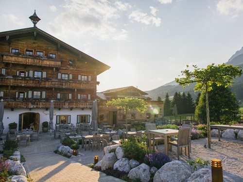 Sonnenterrasse mit Blick auf den ehemaligen Bauernhof Embachhof, heute Teil des Hotels, und die Berge im Abendlicht – Naturresort Puradies, Leogang, Salzburger Land Sonnenterrasse mit Embachhof und Bergpanorama, Puradies Leogang