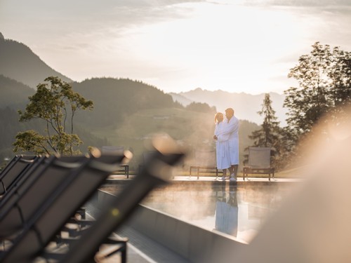 Romantischer Moment am Pool bei Sonnenaufgang – Heaven Spa, Naturresort Puradies, Leogang Paar im Bademantel am Pool bei Sonnenaufgang, Puradies Leogang