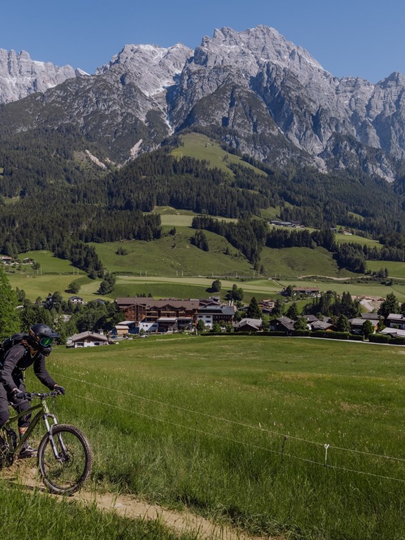 Mountainbiker auf Wiesenpfad, Hotel im Hintergrund, Naturresort Puradies in Leogang