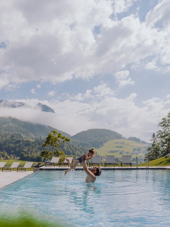 Mann hebt Kind hoch im Infinity Pool im Sommer, Naturresort Puradies, Leogang, Salzburger Land Mann hebt Kind hoch im Infinity Pool im Sommer, Puradies Leogang