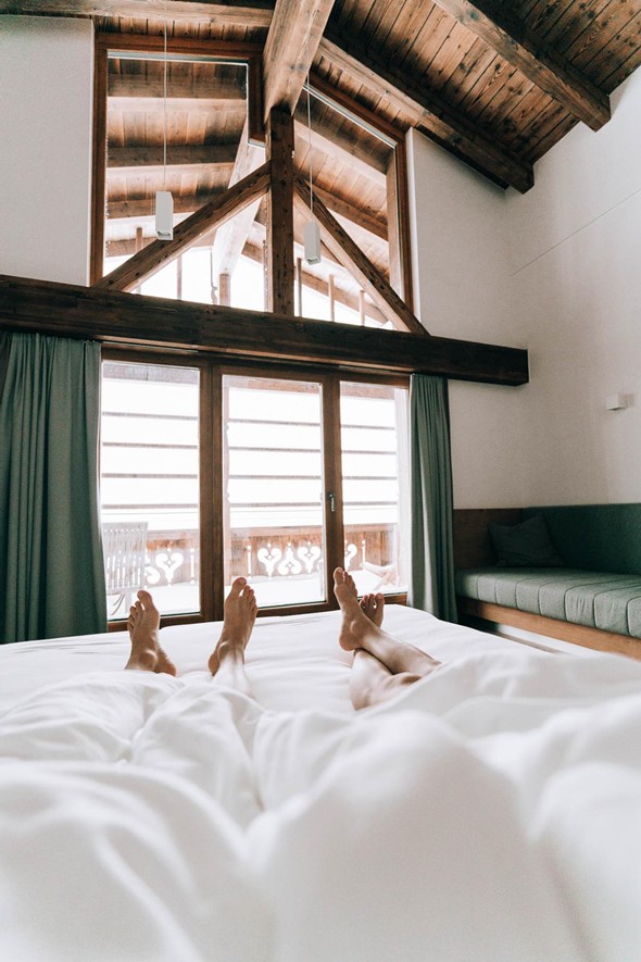 Personen im Bett mit Blick auf Balkon im Winter – Naturresort Puradies, Leogang, Salzburger Land Personen im Bett mit Winterblick auf Balkon, Puradies Leogang